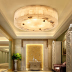 Round Clérachic alabaster ceiling light glowing in a recessed cove ceiling, above a hallway with columns and a gold wall panel.