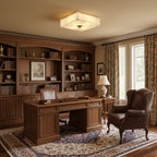 Square Clérachic alabaster ceiling light glowing above a study with wooden bookshelves, a leather armchair and a walnut desk.