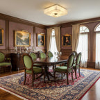 A Clérachic square alabaster ceiling light glows over a dining table with green chairs, framed paintings and a red rug.