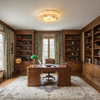 Distant view of a round Clérachic alabaster ceiling light in a wood-panelled study with a desk, green lamp and bookcases.