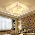 Large square Clérachic alabaster ceiling light in a recessed ceiling above a bed with a diamond-quilted headboard.