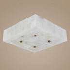 Underside of a square Clérachic alabaster ceiling light, showing the tiled stone sides and four brass studs on a taupe backdrop.