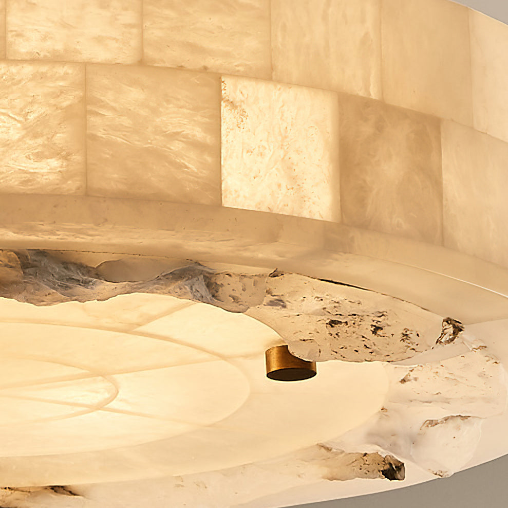 Close view of the tiled alabaster rim, rough stone edge and a brass stud on this Clérachic ceiling light, lit from within.
