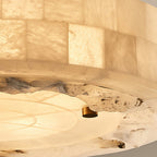 Close view of the tiled alabaster rim, rough stone edge and a brass stud on this Clérachic ceiling light, lit from within.