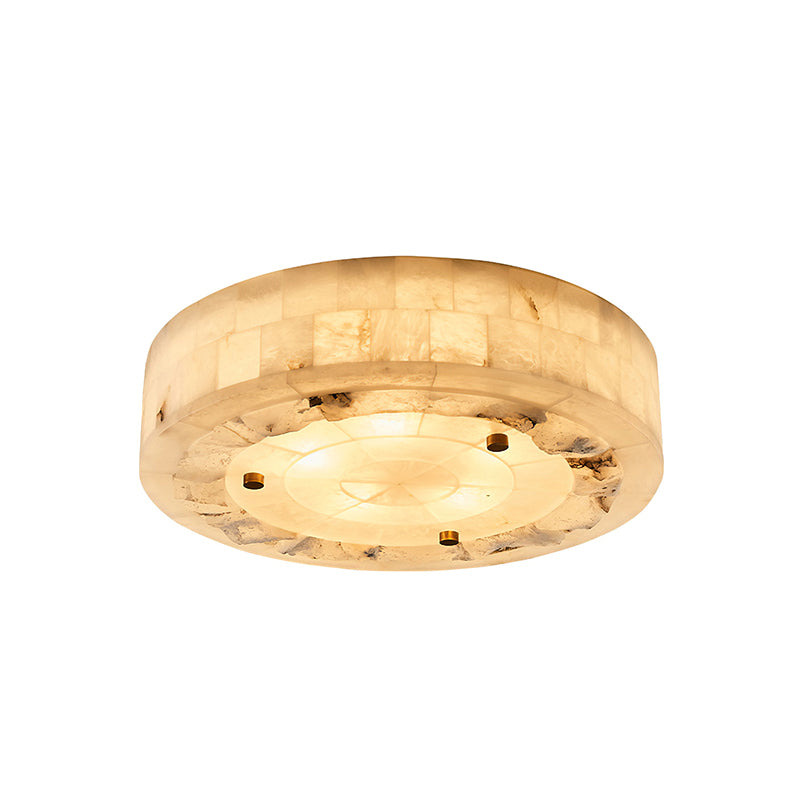 Angled view of a round Clérachic alabaster ceiling light, lit, showing three brass studs and a rough stone ring around the base.