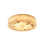 Angled view of a round Clérachic alabaster ceiling light, lit, showing three brass studs and a rough stone ring around the base.