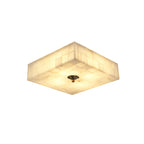 Smaller square alabaster ceiling light from Clérachic, lit, with a single brass centre cap on its tiled underside, on white.