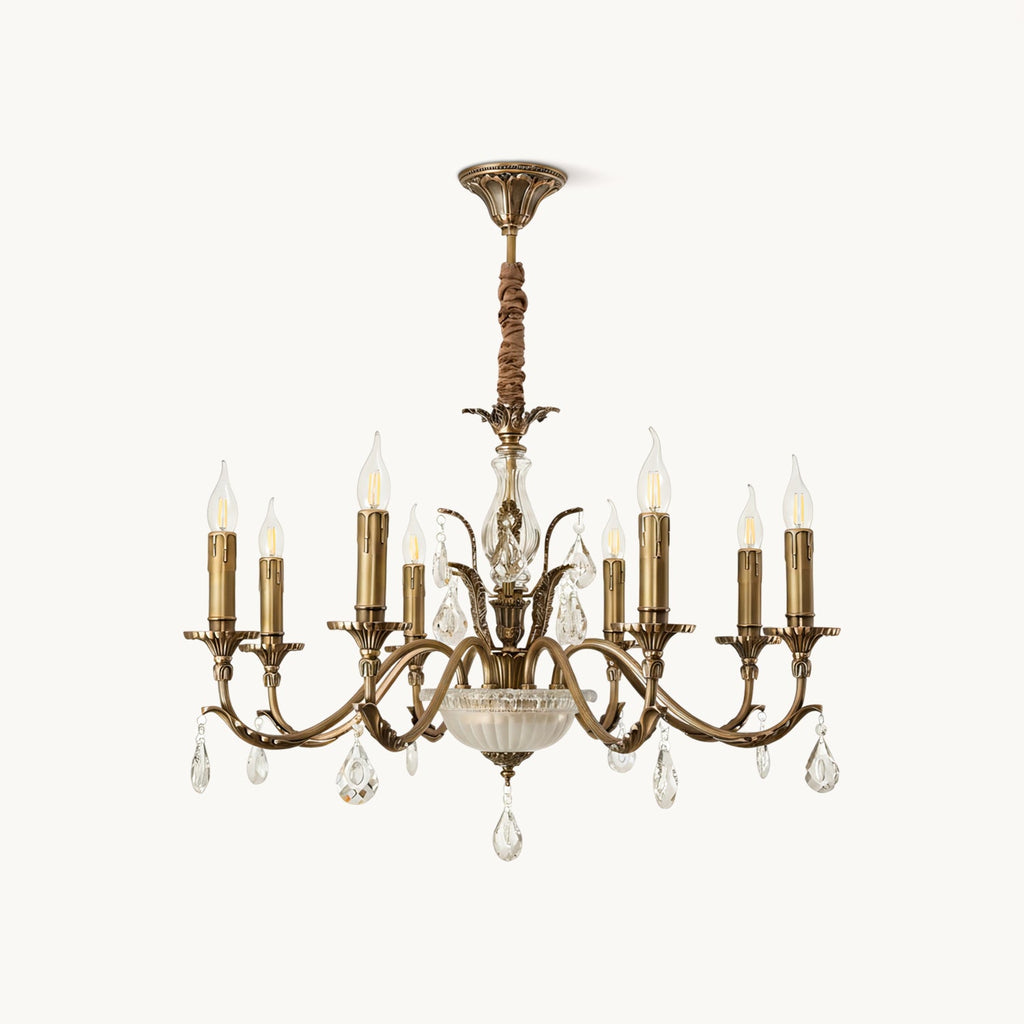 This Clérachic antique brass chandelier on a plain white backdrop, with curving arms, candle-style lights and hanging crystal drops.