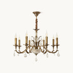 This Clérachic antique brass chandelier on a plain white backdrop, with curving arms, candle-style lights and hanging crystal drops.