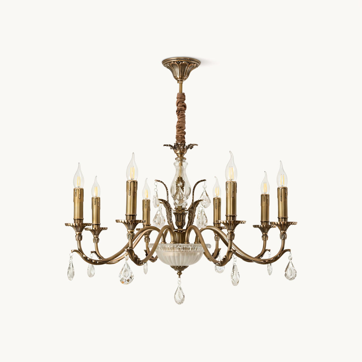 This Clérachic antique brass chandelier on a plain white backdrop, with curving arms, candle-style lights and hanging crystal drops.
