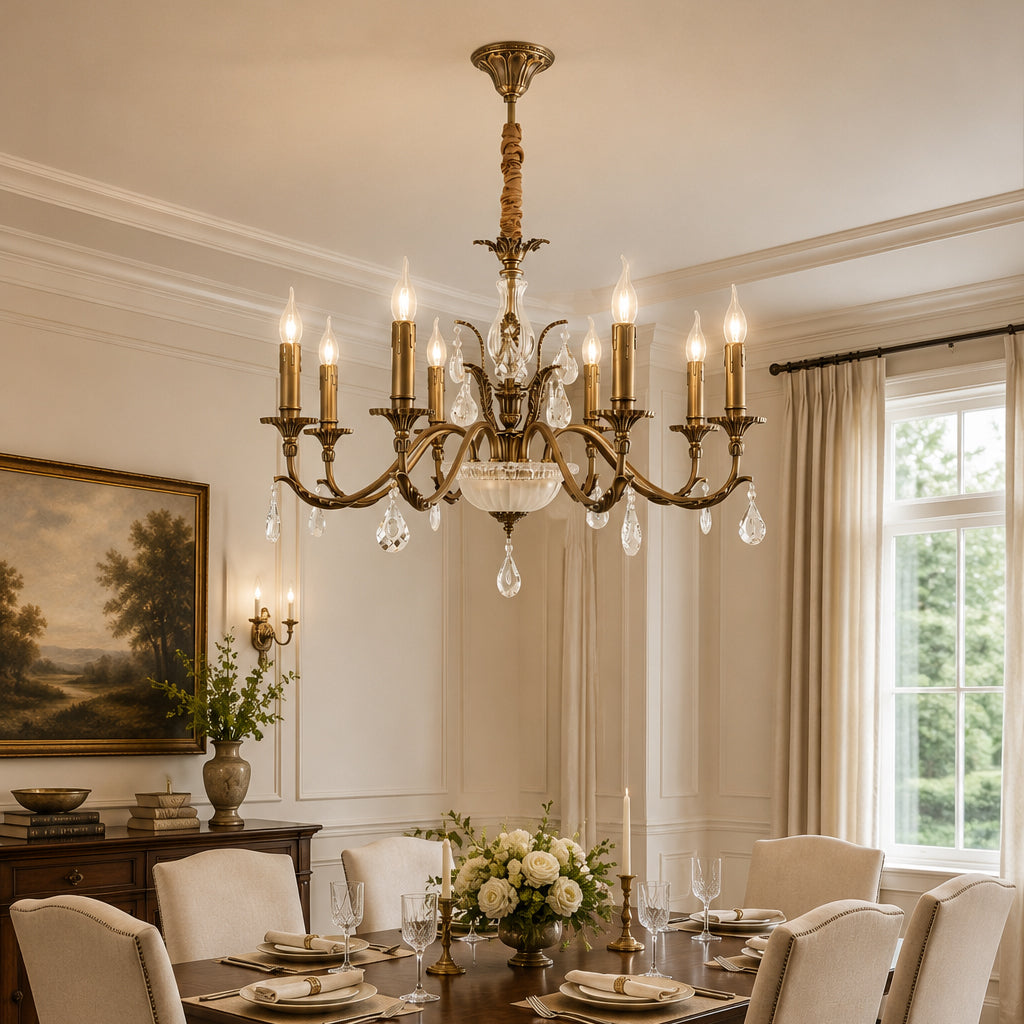 Above a laid dining table in a cream room, a Clérachic antique brass chandelier hangs beside a landscape painting and a tall window.