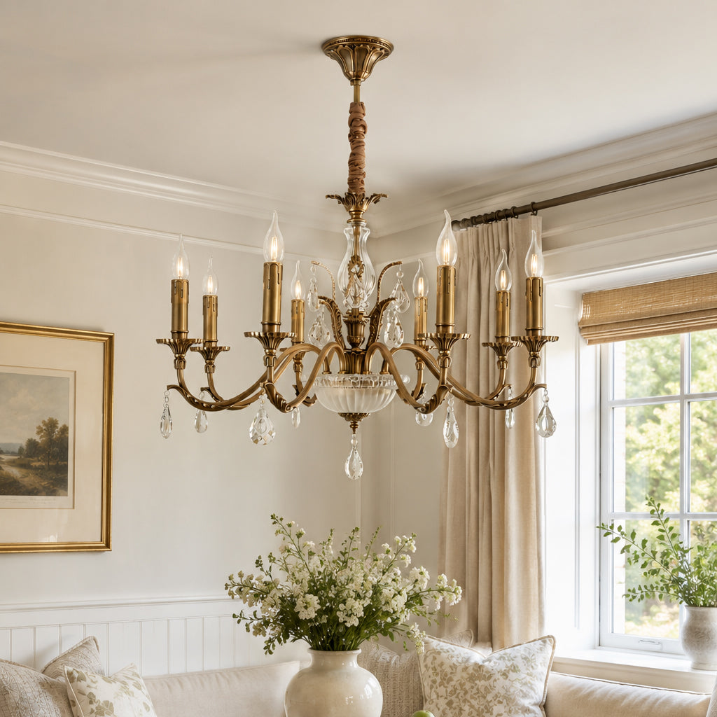 A Clérachic antique brass chandelier hangs in a panelled room, with a vase of white flowers and sheer curtains at the window.
