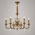 This Clérachic antique brass chandelier on a grey backdrop shows its curved arms, candle lights, glass bowl and crystal drops.
