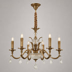 This Clérachic antique brass chandelier on a grey backdrop shows its curved arms, candle lights, glass bowl and crystal drops.