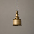 Unlit, the antique brass shade and turned finial of this Clérachic pendant hang against a warm grey backdrop.