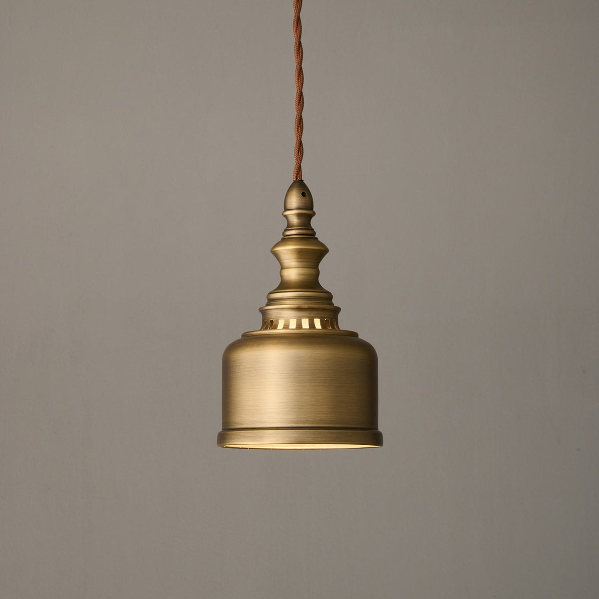 Side view of the brushed brass bell shade and slotted collar of this Clérachic pendant, hanging unlit on its cord.