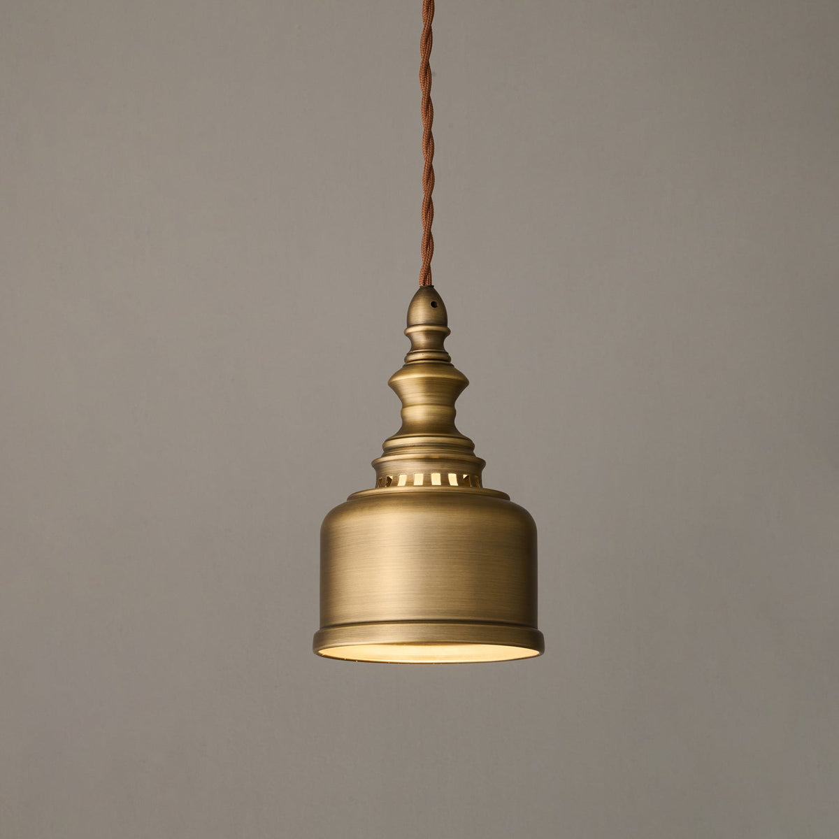 Smaller in the frame, this Clérachic brass dome pendant glows softly from within, its twisted cord running up out of view.
