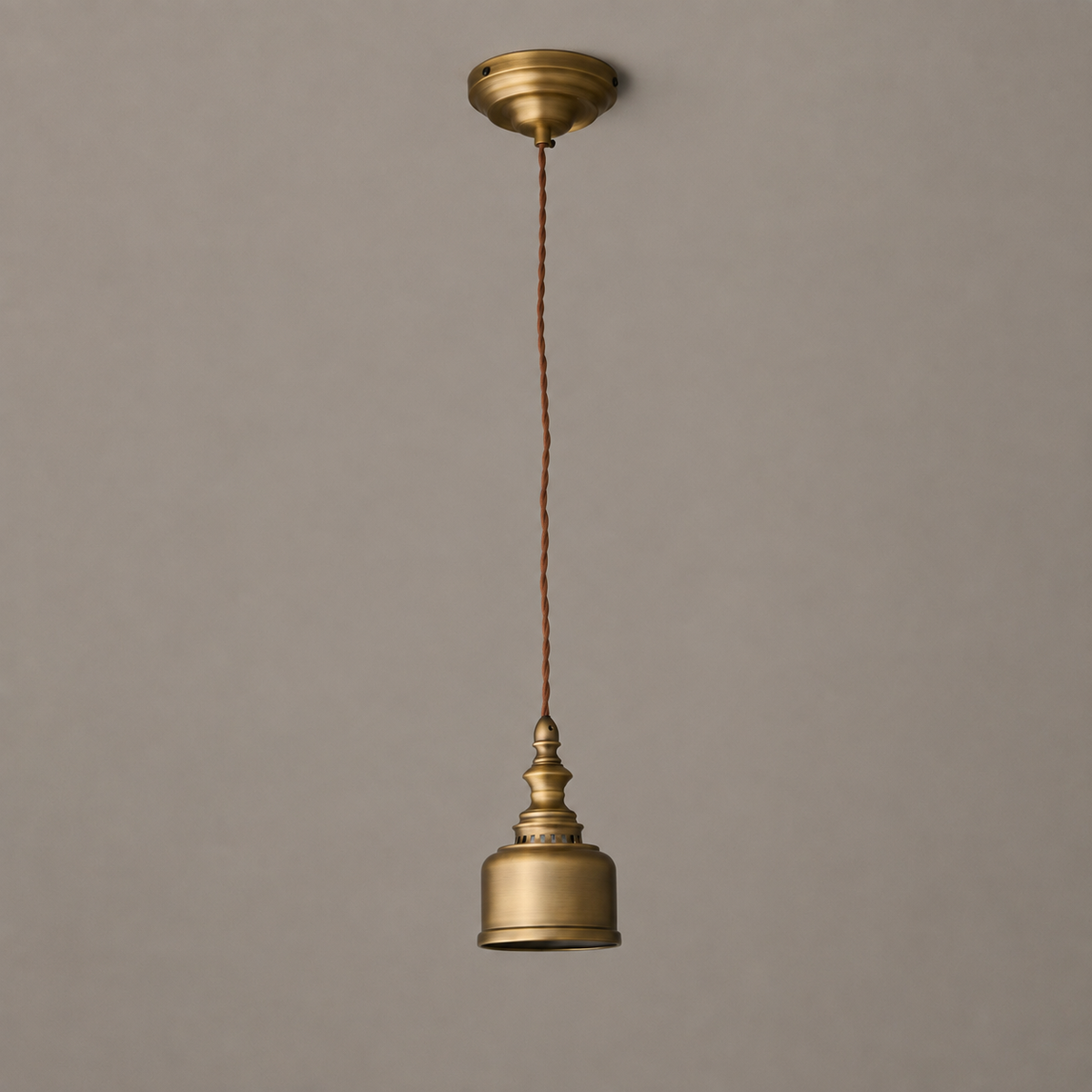 Full drop of a Clérachic brass pendant, from the round brass ceiling canopy down the twisted cord to the unlit dome.