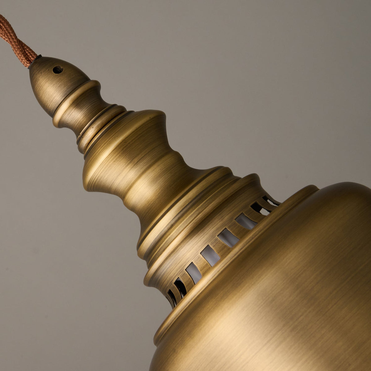 Close view of the turned finial and the slotted ventilation collar where the cord meets this Clérachic brass shade.