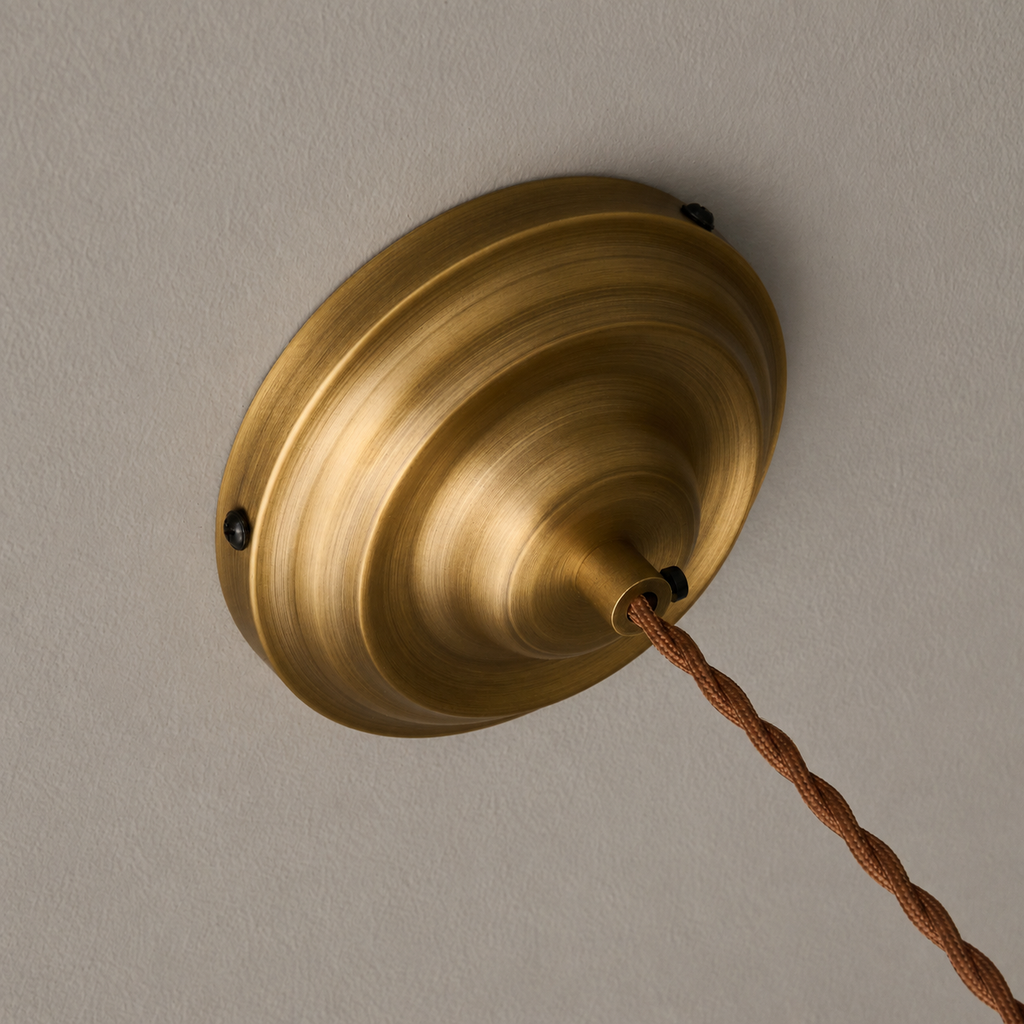 Underside of the round brass canopy on this Clérachic pendant, with two small screws and the twisted brown cord leaving it.