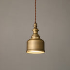 A Clérachic antique brass dome pendant glowing warm on a twisted cord against a soft grey wall, shown at a gentle angle.