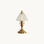 A Clérachic table lamp on a plain off-white backdrop, with an antique brass base and a clear ribbed glass cone shade.