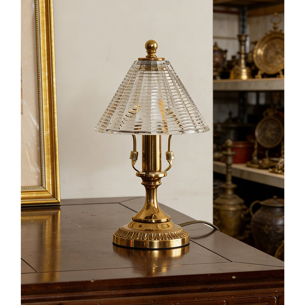 This Clérachic table lamp switched off on a wooden table, with a thin cord trailing from its footed antique brass base.