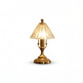 Lit Clérachic table lamp cut out on a white background, showing the warm glow through its clear glass cone shade and brass base.