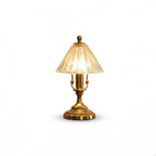 Lit Clérachic table lamp cut out on a white background, showing the warm glow through its clear glass cone shade and brass base.