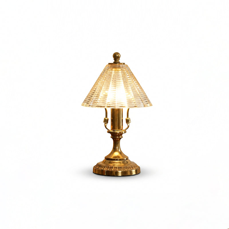 Lit Clérachic table lamp cut out on a white background, showing the warm glow through its clear glass cone shade and brass base.