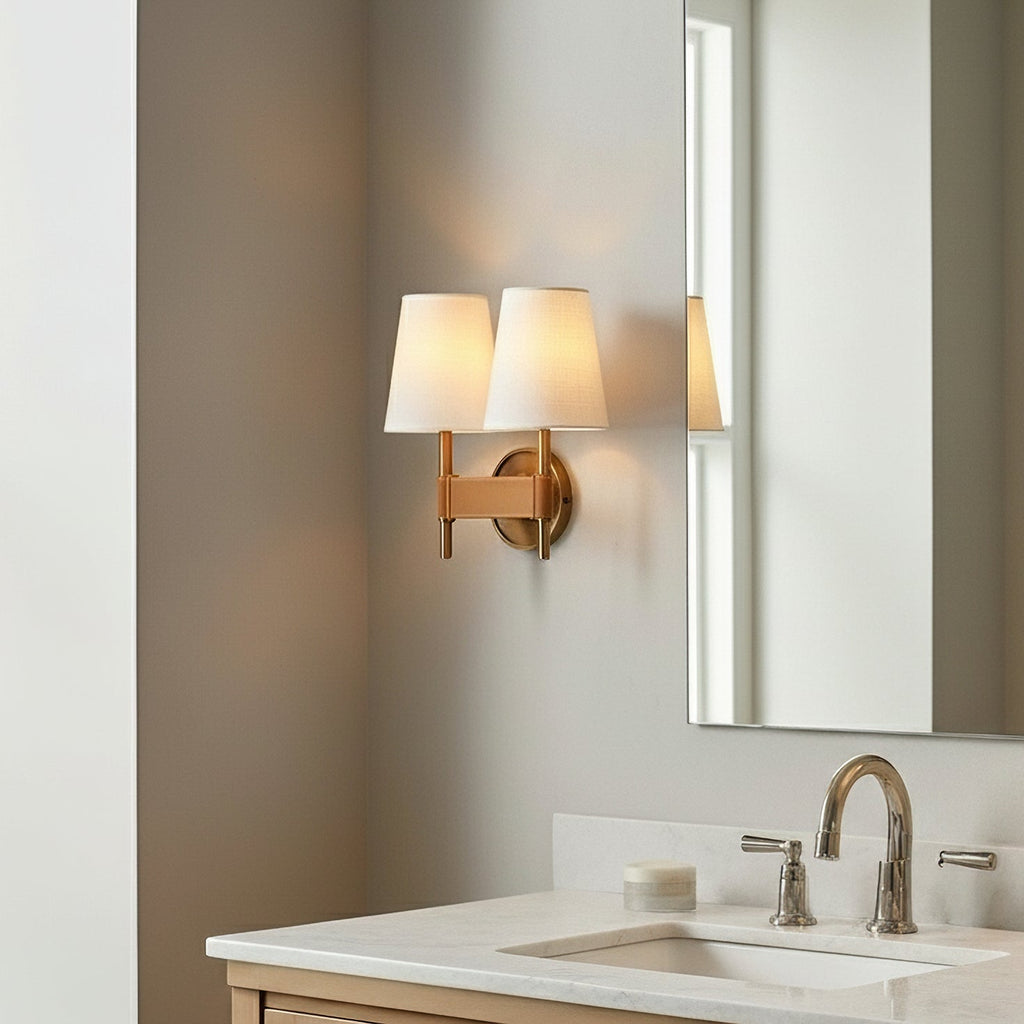A pair of white fabric shades on one Clérachic double wall light, lit warmly beside a tall mirror over a bathroom basin.