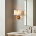 A pair of white fabric shades on one Clérachic double wall light, lit warmly beside a tall mirror over a bathroom basin.