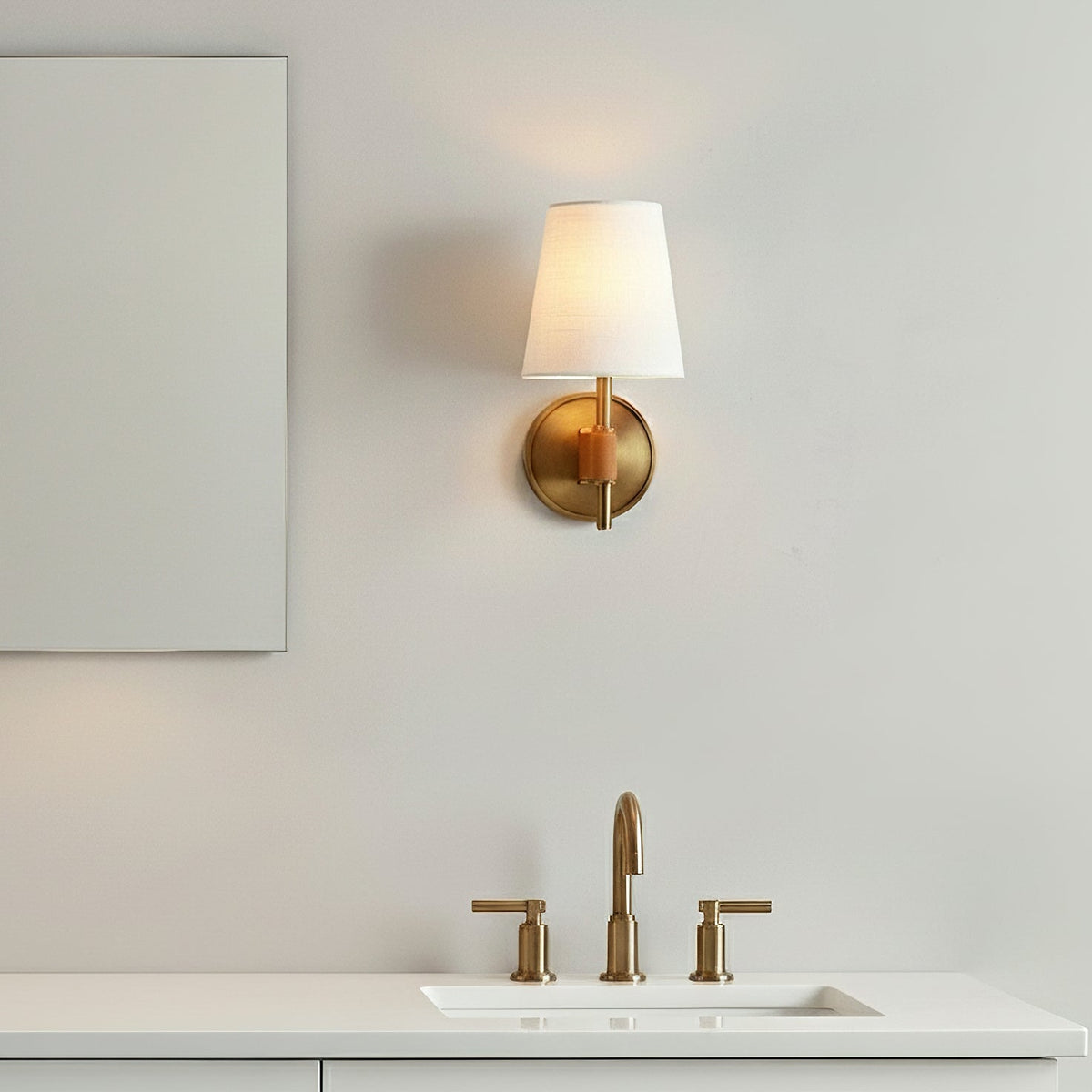 Single Clérachic wall light with a lit white shade above a basin with brass taps, on a pale grey wall.