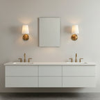 Two single Clérachic wall lights placed either side of a small mirror above a floating double vanity with brass taps.