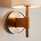 Close view of the brass backplate, stem and tan strap on this Clérachic wall light, with the underside of the lit shade above.