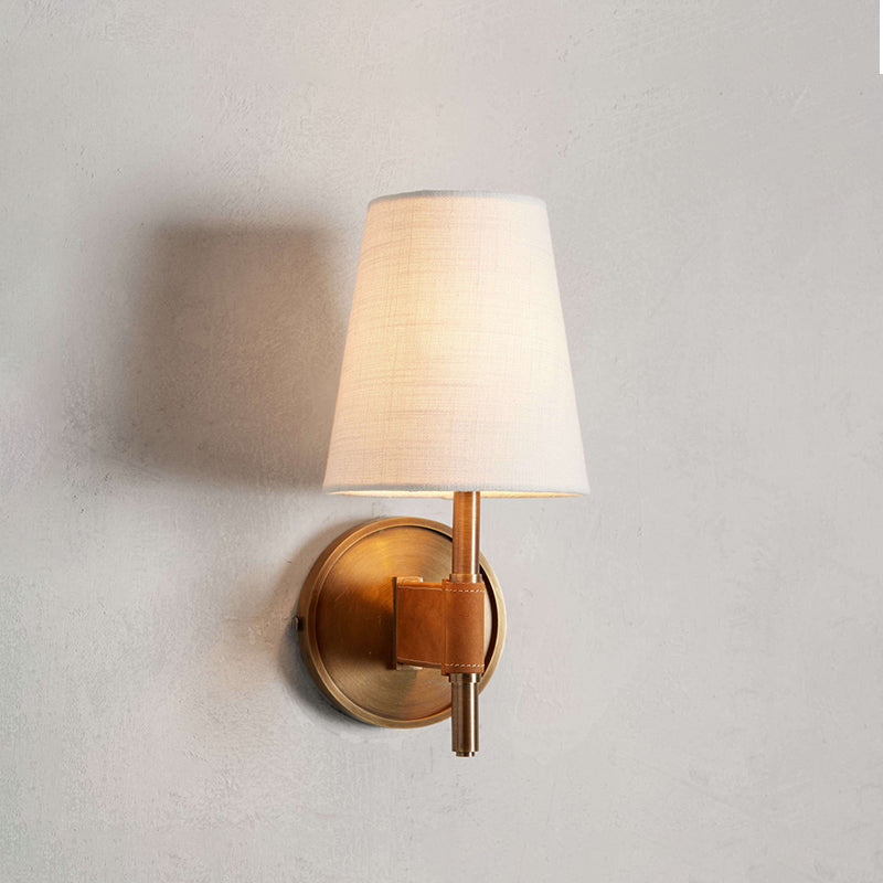 Single Clérachic wall light glowing on a grey plaster-look wall, with a cream shade and a small antique brass backplate below.