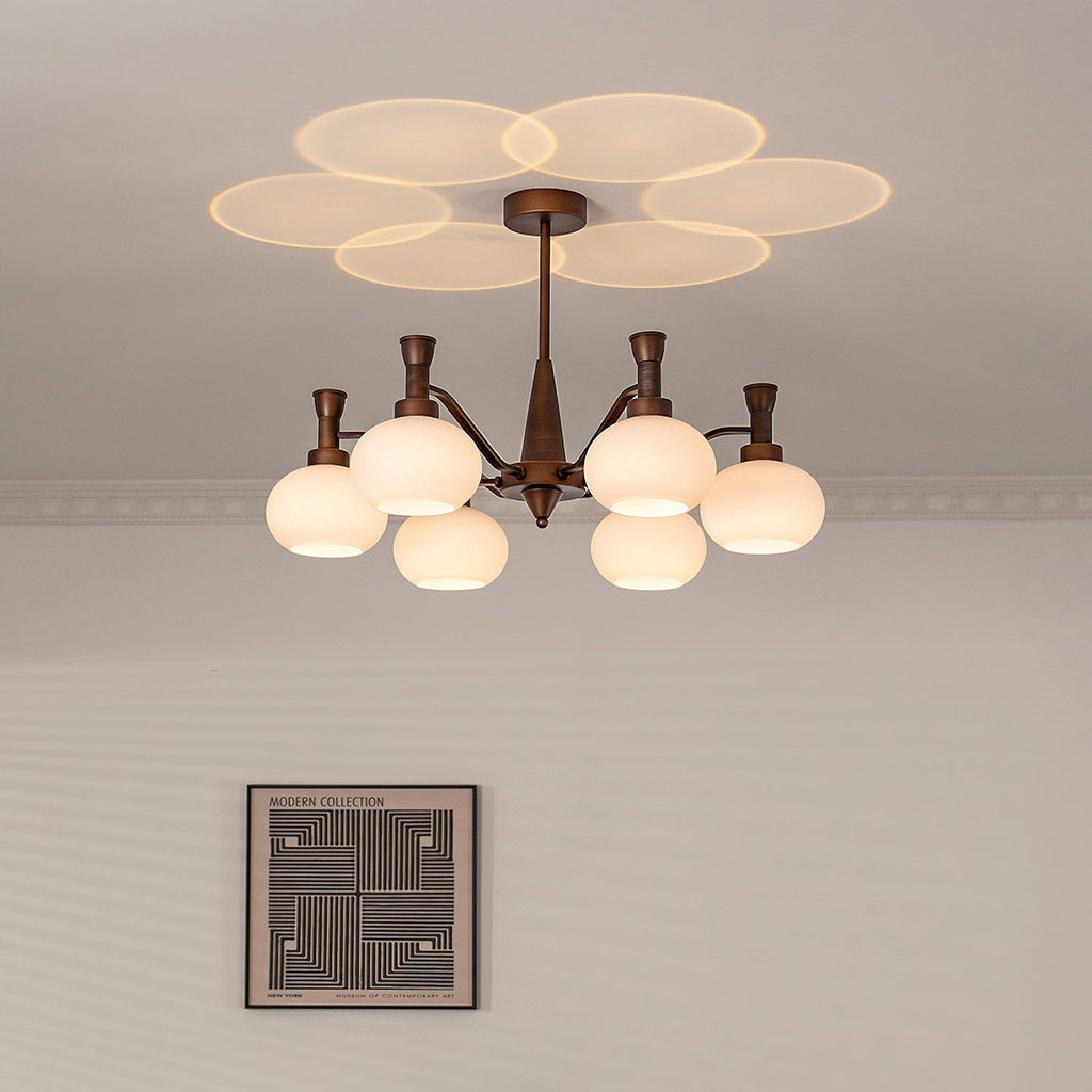 Cream glass shades glowing on this Clérachic chandelier, with a ring-shaped glow on the ceiling and a single framed print on the wall below.