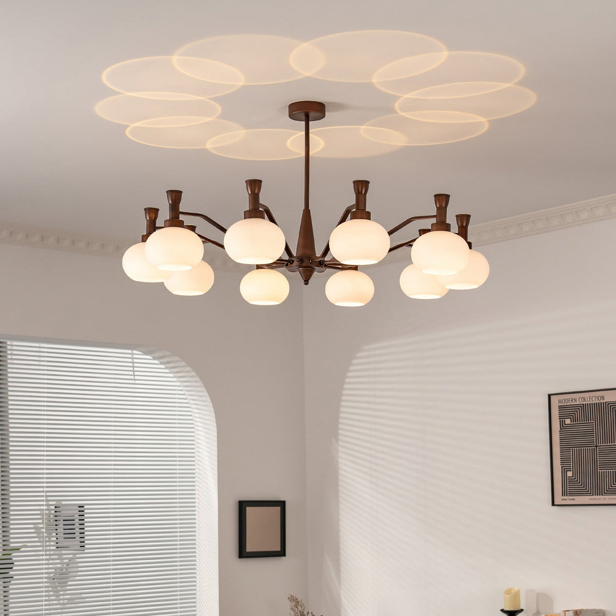 This Clérachic chandelier lit in a corner room with arched openings and slatted blinds, its glass shades casting a petal pattern on the ceiling.