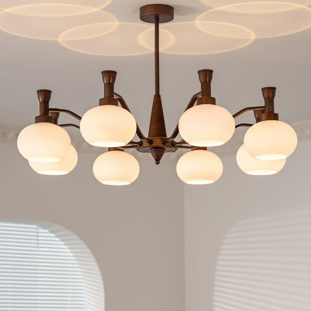 Close, low view of this Clérachic chandelier, its cream glass globes lit and its slim bronze stem rising to a patterned ceiling glow.