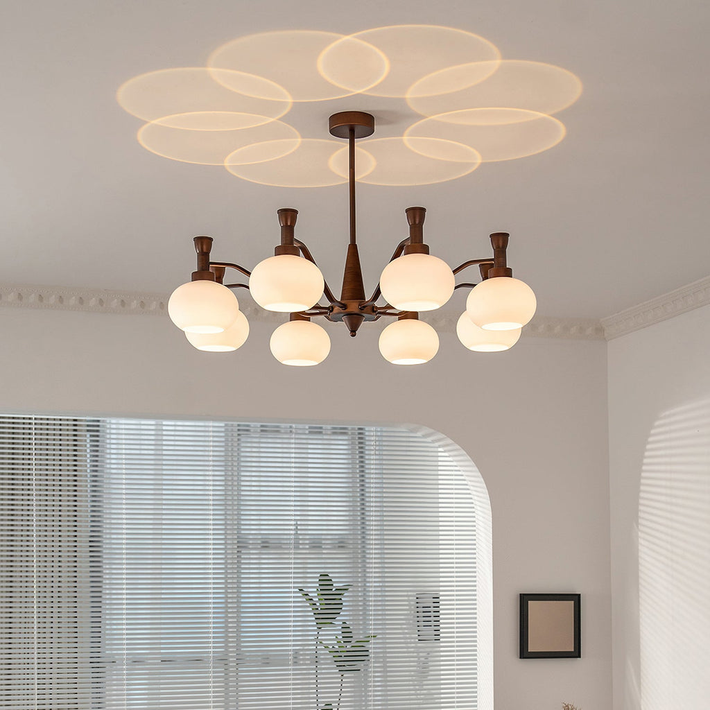 Under a ceiling washed with overlapping light circles, this Clérachic chandelier hangs near a window with blinds and a small framed picture.