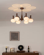 A Clérachic antique bronze chandelier lit above a wall print and a wooden sideboard holding a record player and a bottle.