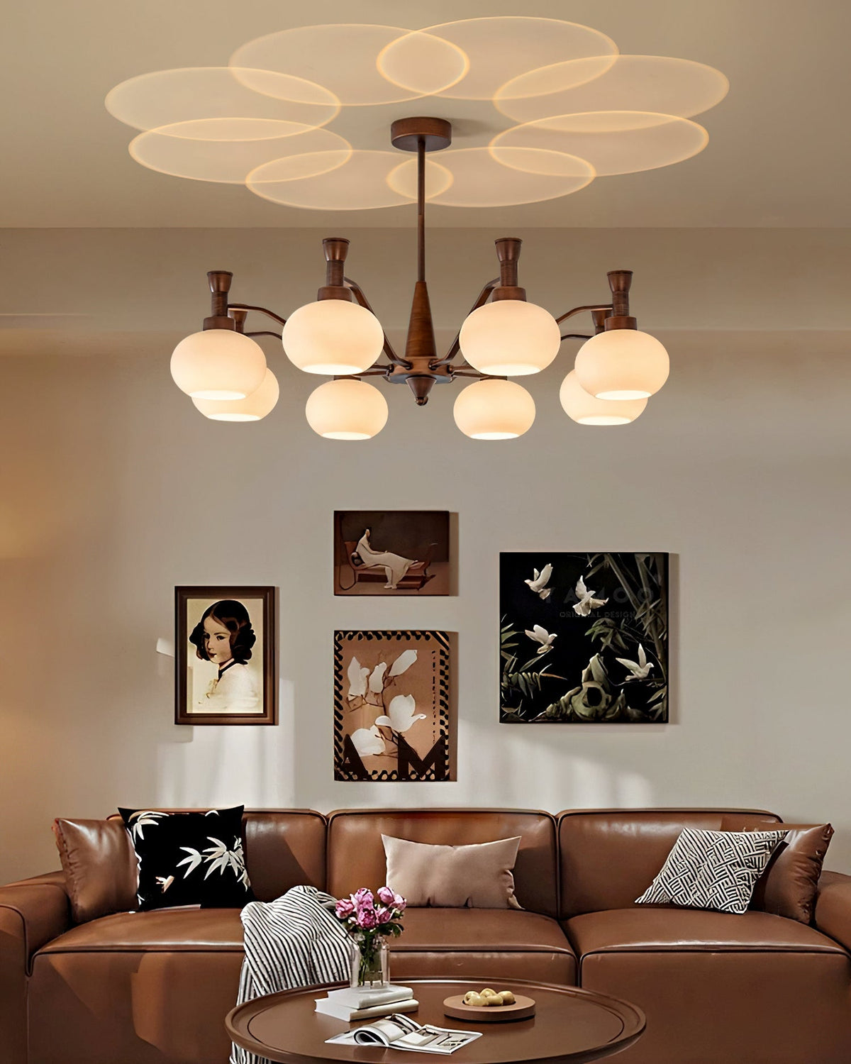 Clérachic chandelier lit above a brown leather sofa and round coffee table, with a gallery of framed pictures on the wall behind.