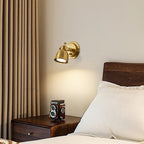 A Clérachic wall light glowing warm beside a walnut bed, with a cream pillow and curtain and a vintage camera on the bedside table.