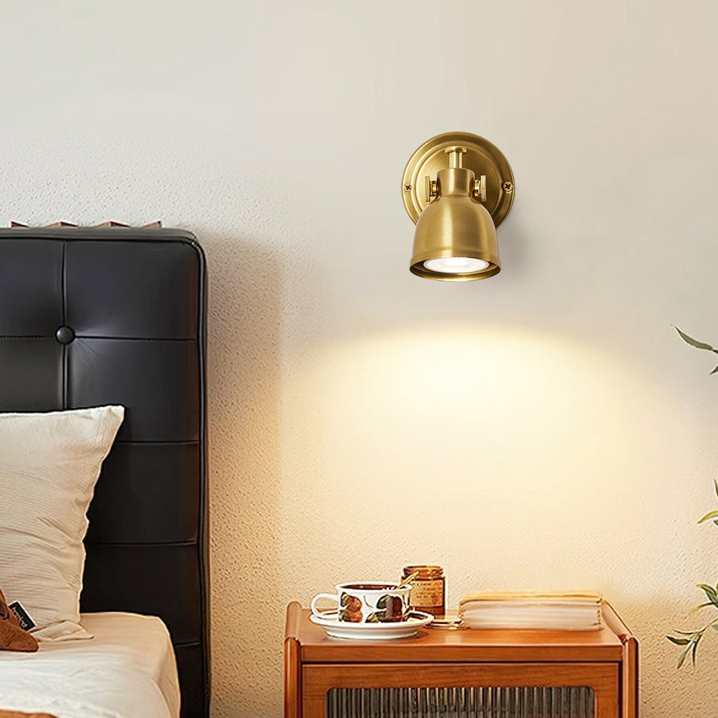 Clérachic wall light mounted above a dark leather headboard, casting a pool of warm light down the wall over a wooden bedside table.