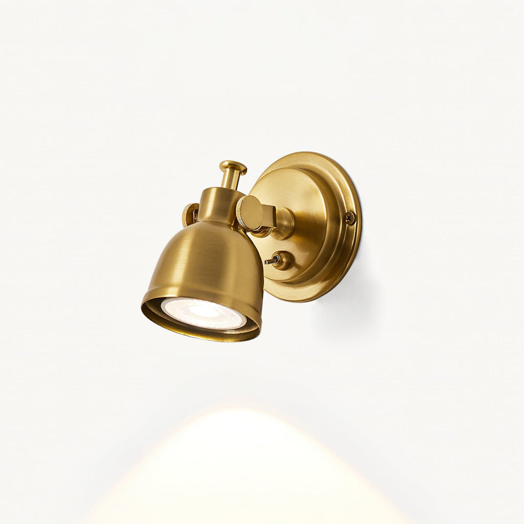 Clérachic wall light on a cream wall with the shade turned to the side, a narrow beam of warm light falling from the bulb below.