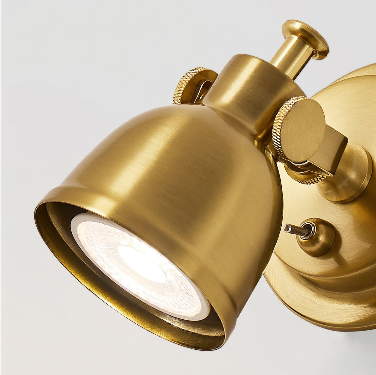 Close view of the brushed brass dome and knurled adjusting screws on this Clérachic wall light, with the lit bulb inside the shade.