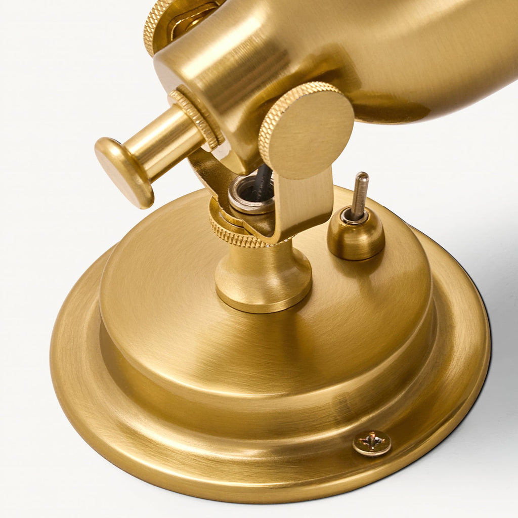 Close view of the swivel joint, knurled knobs, toggle switch and screwed round backplate on this Clérachic antique gold wall light.