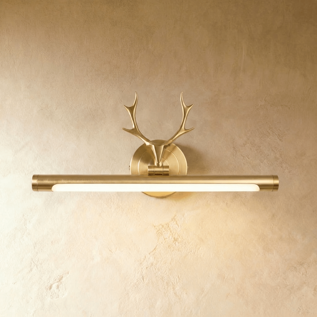 Clérachic brushed brass picture wall light with a stag-antler mount and a lit 43 cm tube, against a warm limewash wall.