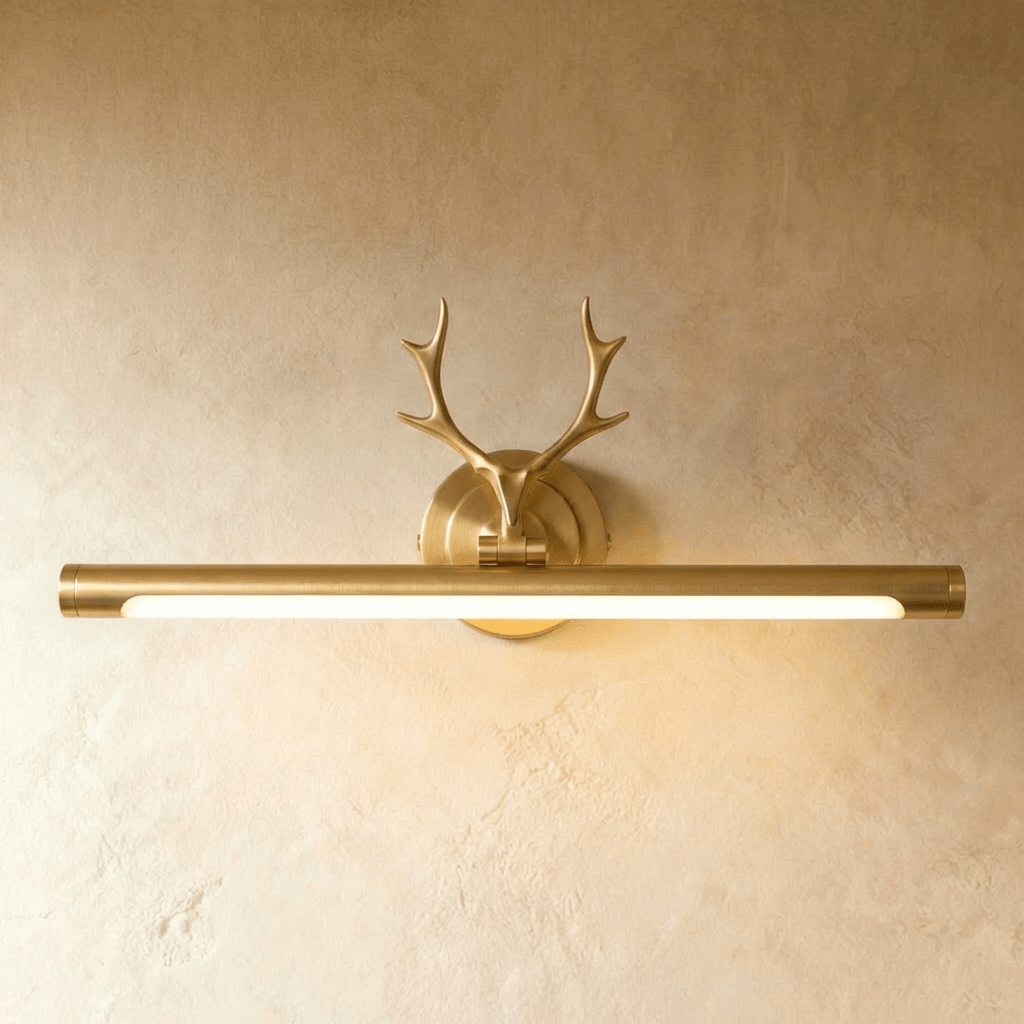 Clérachic brushed brass picture wall light with antler ornament and a longer lit 55 cm tube, on a warm plaster wall.