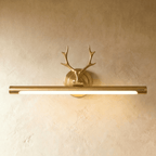 Clérachic brushed brass picture wall light with antler ornament and a longer lit 55 cm tube, on a warm plaster wall.